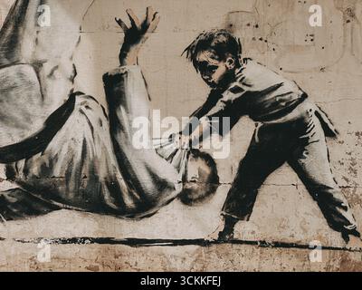 Borodyanka, Ucraina 1 maggio 2025 Banksy illustrazione di un bambino e un uomo che lottano. L'illustrazione raffigura un bambino in un karate gi apparentemente lottando contro un uomo. Un graf Foto Stock