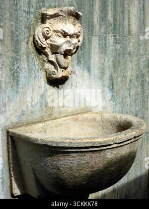 La fontana in pietra ornata di Lisbona presenta un volto di una figura mitologica a bocca aperta, che funge da beccuccio d'acqua. Il bacino intemprato è semicircolare Foto Stock