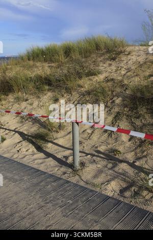 Una spiaggia con una passerella di legno tra le dune di sabbia e una recinzione a strisce rosse e bianche è allungata tra pali di cemento per una maggiore protezione Foto Stock
