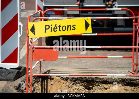 Barriere bianche e rosse con un cartello pedonale giallo su un cantiere stradale urbano. Uno degli scatti verticali sottolinea la presenza imponente delle barriere di sicurezza. Pietons - pedoni. Foto Stock