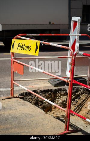 Barriere bianche e rosse con un cartello pedonale giallo su un cantiere stradale urbano. Uno degli scatti verticali sottolinea la presenza imponente delle barriere di sicurezza. Pietons - pedoni. Foto Stock