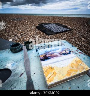 Un dipinto ad olio in corso en-plain-air su una spiaggia. Accanto al lavoro creato su un pannello di legno sospeso viene mostrato un coltello palato Foto Stock