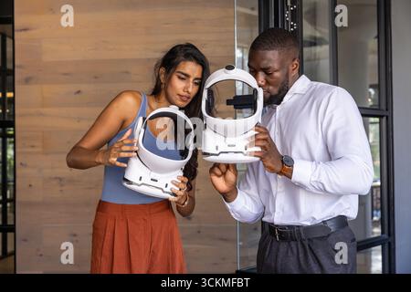 Diversi colleghi che ispezionano il visore vr in ufficio con pareti rivestite in legno Foto Stock