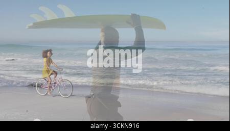 Uomo vestito di muta che porta tavola da surf, donna in abito giallo che pedala in bicicletta sulla spiaggia, onde dell'oceano Foto Stock