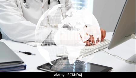 Medico di digitazione che indossa cappotto e stetoscopio sulla scrivania dell'ufficio, con tastiera, monitor e sovrapposizione a globo Foto Stock