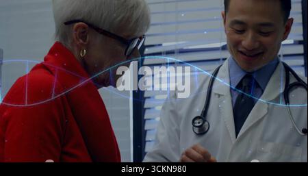 Indica un medico asiatico con stetoscopio che utilizza una compressa consultando un paziente in clinica con elica di DNA Foto Stock