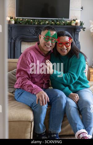 Sorridendo diverse coppie anziane nell'albero delle vacanze e occhiali da corna sedute sul divano accanto al caminetto Foto Stock