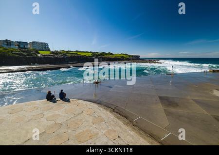 Vista rilassante di una tranquilla piscina costiera con onde oceaniche infranti e splendidi paesaggi. Una coppia gode della tranquillità insieme, creando un ambiente sereno Foto Stock