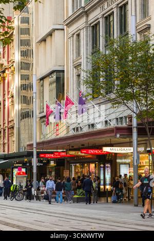 Una vivace strada cittadina caratterizzata da pedoni affollati, punti vendita e un'atmosfera dinamica che rappresenta la vita metropolitana. Architettura iconica e Foto Stock
