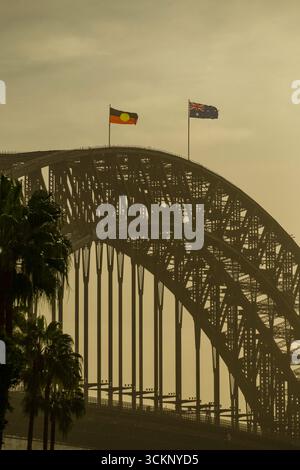 Splendido Sydney Harbour Bridge adornato da bandiere australiane e aborigene, che si stagliano contro un cielo dorato al tramonto. La scena evoca sentimenti Foto Stock