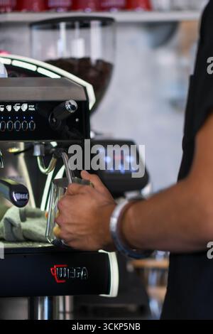 Cremona, Italia - 19 luglio 2025 il barista esperto cuoce con cura il latte in caraffa metallica utilizzando una macchina da caffè professionale in una vivace caffetteria EN Foto Stock