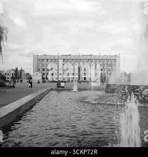 Una vista panoramica della piazza centrale della Rivoluzione d'ottobre (ora Piazza Soborna) a Sloviansk durante la celebrazione della giornata della città nel 1988. In primo piano è attiva una fontana dove i cittadini si rilassano, mentre sullo sfondo si erge un monumentale edificio amministrativo e un monumento di Lenin. Questa immagine è un simbolo della vita pacifica e prospera nel Donbas durante l'era sovietica, catturando il luogo principale per eventi pubblici e per il tempo libero molto prima dei tragici eventi del XXI secolo Foto Stock