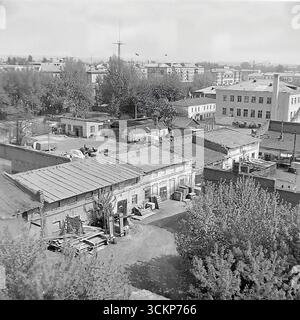 Una vista non cerimoniale dei cortili interni e degli edifici di servizio dietro la piazza centrale della Rivoluzione d'ottobre a Sloviansk, 1970. Queste foto panoramiche mostrano il "backstage" nascosto della città con i suoi vecchi edifici, le officine e i garage, in contrasto con i grattacieli sovietici sullo sfondo. Le cornici illustrano la vera vita quotidiana di una città sovietica e fungono da simbolo del complesso ma pacifico tessuto urbano del Donbas prima che iniziassero i tragici eventi Foto Stock