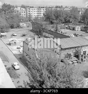 Una vista non cerimoniale dei cortili interni e degli edifici di servizio dietro la piazza centrale della Rivoluzione d'ottobre a Sloviansk, 1970. Queste foto panoramiche mostrano il "backstage" nascosto della città con i suoi vecchi edifici, le officine e i garage, in contrasto con i grattacieli sovietici sullo sfondo. Le cornici illustrano la vera vita quotidiana di una città sovietica e fungono da simbolo del complesso ma pacifico tessuto urbano del Donbas prima che iniziassero i tragici eventi Foto Stock