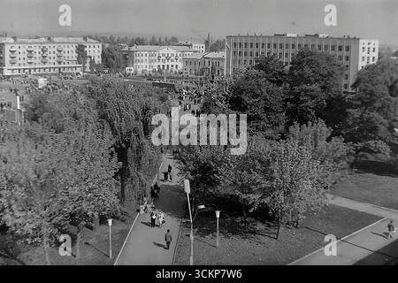 Viste panoramiche della piazza centrale della Rivoluzione d'ottobre (ora piazza Soborna) a Sloviansk, 1976, durante una grande festa pubblica. Migliaia di cittadini sono visti rilassarsi e passeggiare attraverso la piazza verdeggiante sullo sfondo di edifici amministrativi e residenziali. Questi scatti sono un potente simbolo della vita sociale pacifica, ordinata e vibrante nel Donbas durante l'era della stagnazione, catturando lo spirito della comunità della città molto prima dei tragici eventi che hanno distrutto questa esistenza idilliaca Foto Stock