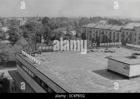 Vista panoramica del grande magazzino Yubileyniy (Jubilee) a Sloviansk, 1976. L'edificio in stile modernista sovietico sulla Piazza della Rivoluzione d'ottobre (ora Piazza Soborna), che include una vista del suo tetto con un cartello parzialmente smantellato contro un paesaggio industriale. Gli scatti riflettono la vita quotidiana e l'architettura dell'era della stagnazione, simboleggiando la vita tranquilla e attiva a Donbas, dove il negozio centrale era un punto di attrazione per i cittadini Foto Stock