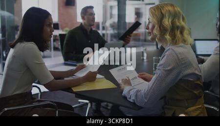 Revisione dei referti stampati quattro professionisti si riuniscono al tavolo in ufficio, con laptop e cartella Foto Stock