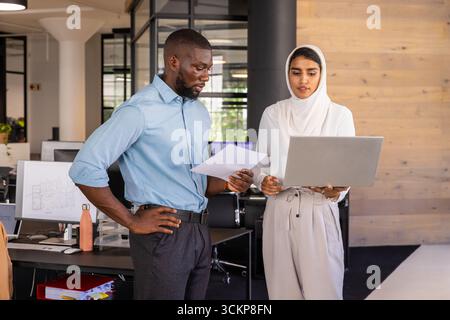 Colleghi diversi in ufficio che esaminano progetti e piani digitali su un notebook color argento Foto Stock