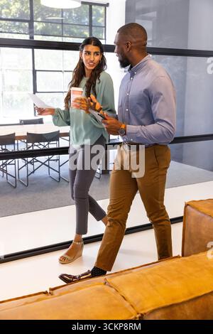 Diversi colleghi di abbigliamento da lavoro che camminano in ufficio, oltre la partizione in vetro che regge il tablet Foto Stock