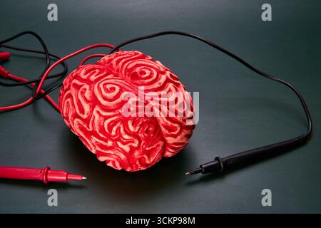 Cervello rosso con elettrodi rossi e neri su una superficie verde. Concetto di mal di testa, emicranie. Foto Stock
