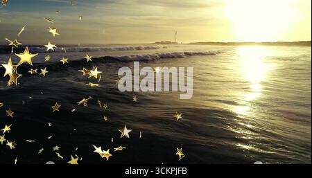 Onde ondulate dell'oceano che riflettono la luce dorata lungo la costa al tramonto, con sovrapposizioni di torri e stelle Foto Stock