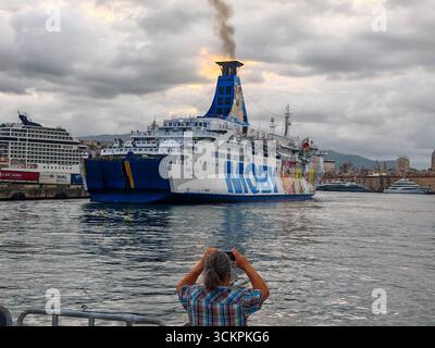 Genova, Italia - 13 settembre 2025: Un turista scatta una foto del traghetto Moby Otta in partenza dal porto di Genova. La nave passeggeri e RoRo gestita dalla compagnia di navigazione Moby collega le città portuali del Mediterraneo e trasporta veicoli *** Ein Tourist fotografiert die Autofähre Moby Otta bei der Abfahrt aus dem Hafen von Genua. DAS Passagier- und RoRo-Schiff der Reederei Moby verbindet Hafenstädte im Mittelmeer und transportiert Fahrzeuge Foto Stock