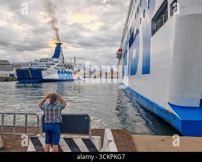 Genova, Italia - 13 settembre 2025: Un turista scatta una foto del traghetto Moby Otta in partenza dal porto di Genova. La nave passeggeri e RoRo gestita dalla compagnia di navigazione Moby collega le città portuali del Mediterraneo e trasporta veicoli *** Ein Tourist fotografiert die Autofähre Moby Otta bei der Abfahrt aus dem Hafen von Genua. DAS Passagier- und RoRo-Schiff der Reederei Moby verbindet Hafenstädte im Mittelmeer und transportiert Fahrzeuge Foto Stock
