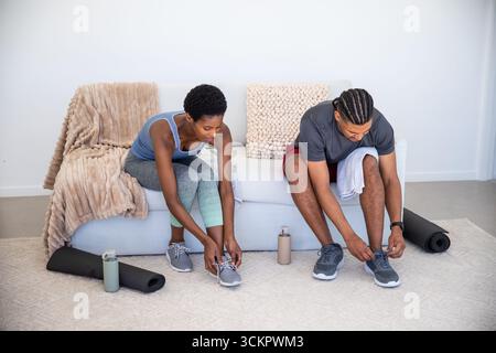 Diverse coppie di scarpe da ginnastica mentre si siedono sul divano nel soggiorno con tappetini per yoga e bottiglie d'acqua Foto Stock