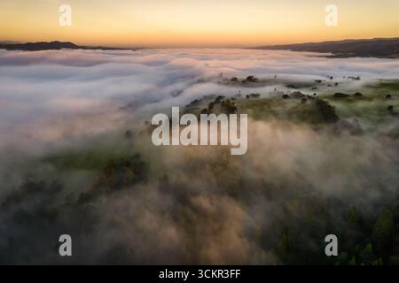 Vista aerea di un paesaggio montano avvolto dalla nebbia mattutina durante l'ora d'oro Foto Stock