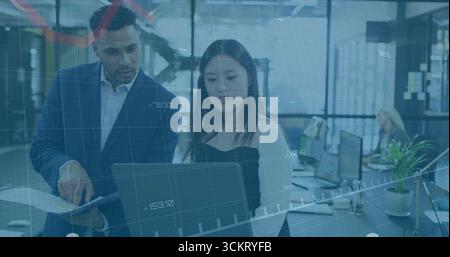 Collaborazione con i colleghi che esaminano il laptop in un ufficio aperto, con report stampati e monitor Foto Stock