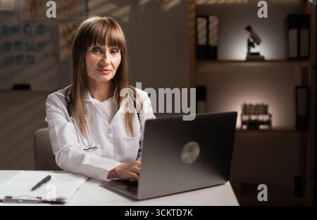 Donna medico o medico di medicina lavoratrice di salute che lavora digitando sul laptop che controlla la storia medica in ospedale o clinica che fa i documenti del paziente. Foto Stock