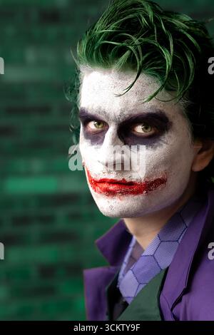 Primo piano ritratto di un giovane cosplayer maschile vestito da Joker con il volto e che guarda direttamente la fotocamera Foto Stock