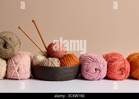 Palline colorate in filato con aghi per maglieria in una ciotola di legno su sfondo neutro Foto Stock
