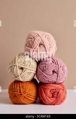 Palline colorate di filato in tonalità pastello e calde impilate su sfondo neutro Foto Stock