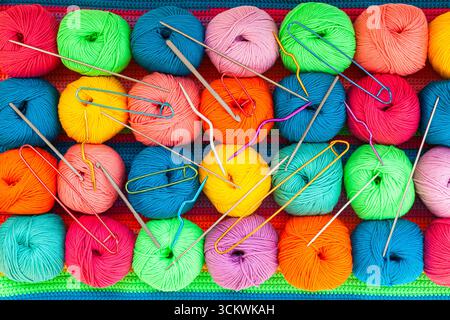 Tutto per maglieria a mano. Tessuto lavorato a maglia multicolore realizzato a mano con sfere di fili multicolori, spille e vari aghi per maglieria. Foto Stock