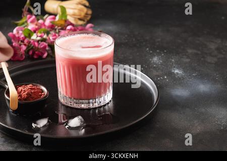 Latte matcha rosa con fiori sakura decorati a polvere su sfondo scuro. Bevanda alla moda. Rinfrescante matcha rosa ghiacciato. Primo piano. Foto Stock