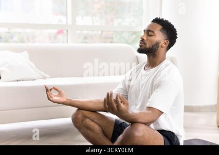 Giovane sportivo calmo seduto sul pavimento a meditare a occhi chiusi Foto Stock