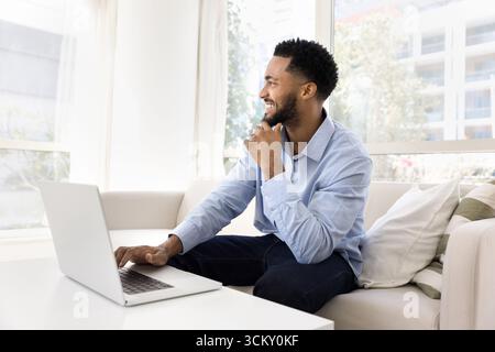 Un giovane freelance da sogno si siede accanto a un notebook in ufficio a casa Foto Stock