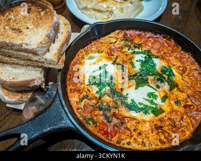 Vista dall'alto dello shakshouka, uova in camicia in salsa di pomodoro servite in una padella con pane su un tavolo da pranzo in un ristorante locale a Riyadh, Arabia Saudita Foto Stock