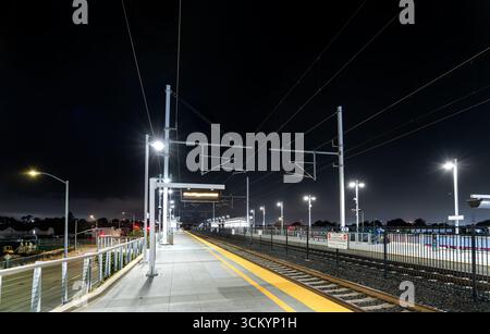 La moderna stazione di Caltrain a San Bruno, California, USA, sulla linea San Francisco - San Jose. La piattaforma vuota è illuminata sotto un cielo notturno buio Foto Stock