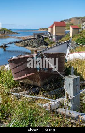 Un dory legato sulla riva con palchi di pesca sullo sfondo vicino a Back Harbour, Terranova Foto Stock