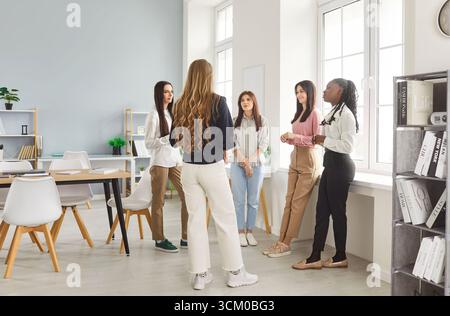 Cinque donne professionali impegnate in un evento di briefing in piedi in cerchio in un ufficio moderno Foto Stock