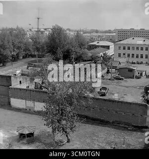 Dietro le quinte di una grande ricostruzione: Vita nei cortili dietro la piazza centrale di Sloviansk, 1975-1976. Lo scatto cattura il caotico mix di vita residenziale, tra cui un parco giochi con gazebo e un'auto sovietica "Zhiguli", continuando nel bel mezzo del grande progetto di rinnovamento della città. Questa fotografia riflette il netto contrasto tra il centro cerimoniale della città e l'autentica vita quotidiana dei suoi abitanti, simboleggiando il mondo pacifico e poliedrico della regione del Donbas, un mondo che esisteva molto prima dei tragici eventi del futuro Foto Stock