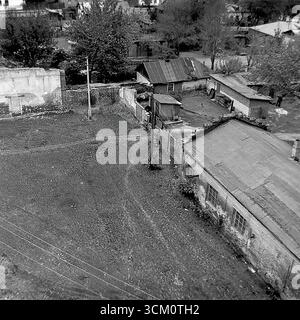 Dietro le quinte di un importante progetto di ricostruzione: Cortili interni caotici e un settore residenziale privato dietro la piazza centrale di Sloviansk, 1975-1976. Il colpo cattura vecchie case in attesa di demolizione, capannoni, detriti. Questa immagine riflette il processo di sdoganamento del sito per il rinnovamento urbano, simboleggiando un'epoca passata sacrificata per la nuova e monumentale visione di una città sovietica, e documenta la complessa ma pacifica vita nel Donbas durante quel periodo Foto Stock