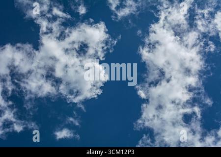 Nuvole bianche sparse intorno a un cielo azzurro vivace che forma un'apertura circolare che crea una scena dinamica e suggestiva Foto Stock