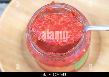 Tradizionale salsa adjika al peperoncino rosso caldo in vaso di vetro con cucchiaio, condimento speziato fatto in casa per cucinare. Foto Stock
