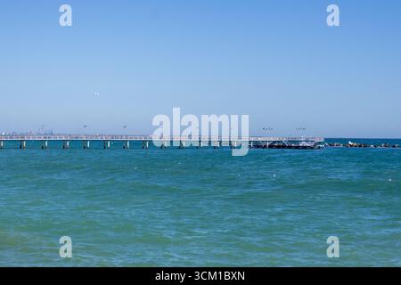 Vista panoramica di un lungo molo che si estende nel mare turchese con un cielo limpido e luminoso. Foto Stock