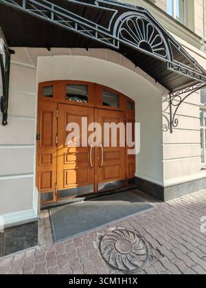 Un'elegante porta in legno con pannelli decorativi in vetro e intagli geometrici, adagiata su una facciata pallida. Questa immagine riflette uno stile architettonico senza tempo e. Foto Stock