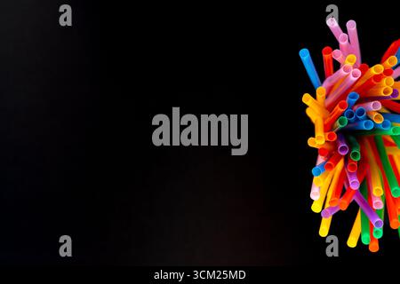 Vista dall'alto verso il basso delle cannucce colorate racchiuse in un contenitore su sfondo nero. Messa a fuoco selettiva e sfondo sfocato con spazio di copia. Foto Stock