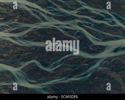 Vista aerea delle trecce glaciali del fiume che serpeggiano attraverso il paesaggio scuro e aspro, un'ipnotica danza di texture e toni contrastanti, Kalfafell, Islanda. Foto Stock